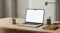 Modern minimalist workspace with open laptop displaying blank white screen on wooden desk. Clean home office setup with coffee mug, notebooks and desk lamp.