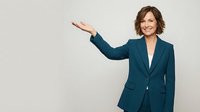 Professional businesswoman in teal suit presenting with open palm gesture, smiling confidently against neutral background for corporate presentations.