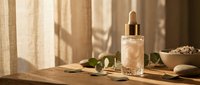 Natural skincare serum bottle with dropper on wooden surface surrounded by green leaves and spa accessories in warm sunlight for beauty routine.