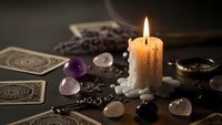 Mystical fortune telling setup with burning candle, tarot cards, crystals and gemstones on dark wooden table for spiritual guidance and divination practices.