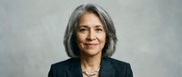 Professional mature Hispanic businesswoman with gray hair smiling confidently in dark suit jacket against neutral background for corporate headshots.