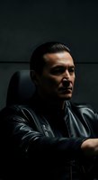 Middle-aged man with dark hair and facial hair wearing black leather jacket, seated against dark background. Suitable for corporate, lifestyle, and portrait projects.