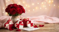 Red roses bouquet in vase with gift boxes and fairy lights creating romantic Valentine's Day or anniversary celebration atmosphere on wooden table.
