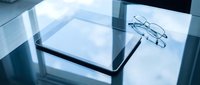 Modern digital tablet with stylish eyeglasses on reflective glass surface in contemporary office workspace for business technology and productivity applications.