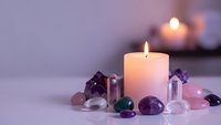 Burning candle surrounded by healing crystals and gemstones creating peaceful meditation atmosphere for wellness and spiritual practices.