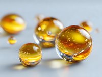 Transparent amber glass marbles with golden reflections on light gray background, macro photography showing liquid-like texture and light refraction effects.
