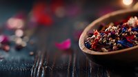 Aromatic dried flower petals and herbs in wooden bowl on dark rustic table with soft moody lighting, selective focus creates dreamy atmosphere for wellness concept.