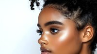 Young African American woman with glowing dewy skin, natural curly hair, and professional makeup in profile view against white background, beauty portrait.