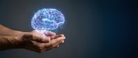 Glowing digital brain hologram floating above cupped hands against dark background representing artificial intelligence, neuroscience and cognitive technology concepts.