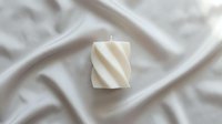Cream-colored twisted pillar candle on white draped fabric background, isolated for home decor, wellness, and aromatherapy design projects.