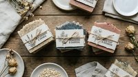Handmade soap bars with kraft paper labels arranged on wooden surface alongside dried flowers, white plates, and natural decorative elements for artisan product photography and wellness branding.