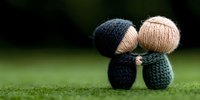 Knitted couple figurines embracing on green grass background, romantic handmade wool dolls showing love and tenderness in minimalist style.