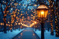Glowing vintage street lamp illuminates snowy winter path with magical bokeh lights and decorations in evening park creating cozy festive atmosphere.