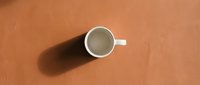 Empty white coffee cup with handle casting shadow on warm terracotta orange surface, minimalist overhead view for kitchen and cafe design concepts.