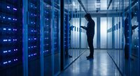 IT technician monitoring server infrastructure in modern data center with blue LED lighting and glass panels for technology solutions.