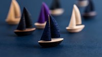 Miniature wooden sailboats with colorful fabric sails arranged on dark blue background, creating depth and perspective in minimal nautical composition.