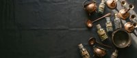 Vintage copper cookware and brass spice containers arranged on dark slate background. Traditional kitchen utensils and storage jars for culinary design projects.