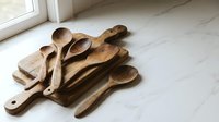 Rustic wooden kitchen utensils and cutting boards arranged on marble countertop near window for cooking and food preparation in modern home interior.