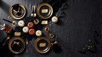 Elegant autumn table setting with golden plates, pumpkins and fall decorations on dark background for Thanksgiving dinner party celebration.