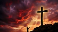 Silhouette of person with raised arms standing before large cross against dramatic sunset sky with vibrant red, orange and purple clouds for spiritual worship concepts.