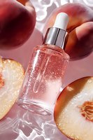 Cosmetic serum bottle with fresh plums and light effects. Pink liquid essence dropper on crystal surface surrounded by cut and whole plums in natural sunlight.