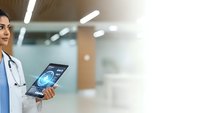 Female doctor in blue scrubs holding digital tablet with medical brain scan in modern hospital corridor for healthcare technology applications.