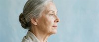Senior woman with gray hair in profile, Caucasian ethnicity, wearing neutral beige clothing against soft blue background. Suitable for healthcare, wellness, aging, and lifestyle editorial use.