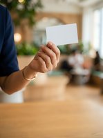Person holding blank white card in modern office environment with wooden table and blurred background, suitable for business branding and corporate messaging.