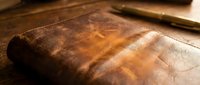 Aged leather-bound book with worn brown cover resting on wooden surface in warm golden light creating nostalgic atmosphere for vintage literature concepts.