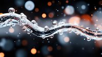 Flowing water wave with transparent spherical droplets against dark background with orange and white bokeh lights creating magical atmosphere.