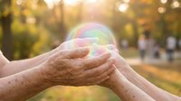 Elderly hands gently holding colorful soap bubble in autumn park with golden sunlight and bokeh background creating magical moment of wonder and joy.