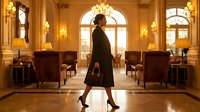 Professional businesswoman walking confidently through luxurious hotel lobby with elegant furniture, warm lighting and classic interior design for corporate success.