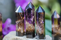 Smoky quartz and amethyst crystal points with natural inclusions standing upright against blurred purple floral background, showcasing mineral formations.