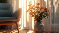 Orange lilies in gray ceramic vase on wooden table near window with sunlight streaming through sheer curtains creating cozy morning atmosphere in modern interior.