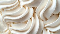 Creamy white meringue swirls create soft waves and curves in close-up view, showing delicate texture and smooth peaks of whipped dessert topping.