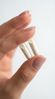 Hand holding two white capsules or pills between fingers on clean background for healthcare and medicine concepts.