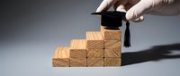 Hand placing graduation cap on wooden blocks arranged as steps representing educational achievement and career advancement concept.