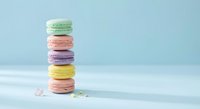 Colorful French macarons stacked in tower on white surface against soft blue background. Pastel dessert treats for bakery menu and sweet confectionery designs.