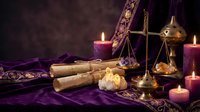 Mystical fortune telling setup with tarot cards, brass scales, burning candles and ancient scrolls on purple velvet fabric for spiritual consultation sessions.