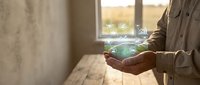 Professional businessman holding glowing green recycling symbol in cupped hands by window, representing environmental responsibility and sustainable business practices.