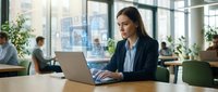 Professional businesswoman working on laptop in modern office space with city view and natural lighting for corporate presentations.