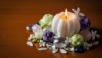 Spa wellness arrangement with lit candle, amethyst crystals, lotus flowers and white petals on warm wooden surface for relaxation and meditation.