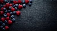 Fresh mixed berries raspberries and blueberries scattered on dark slate stone background with copy space for healthy food and nutrition concepts.