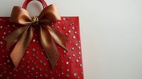 Elegant red gift bag with golden bronze bow and star pattern for holiday shopping and present giving occasions.