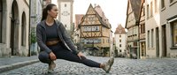 Young woman in athletic wear stretching on cobblestone street in historic European town with traditional half-timbered architecture, fitness and wellness lifestyle concept.