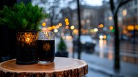 Dark beer glasses on wooden coaster against blurred urban evening background with bokeh lights and rain. Cozy winter atmosphere for restaurant promotion.