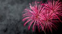 Vibrant pink fireworks exploding against dark night sky, creating festive celebration atmosphere for holiday events and commemorations.