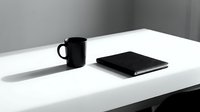 Black mug and notebook on white desk with minimalist workspace setup for business, office, and productivity concepts.