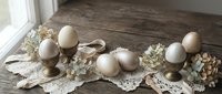 Rustic Easter table setting with natural eggs, vintage lace doilies and dried flowers on weathered wood surface for spring holiday decoration.