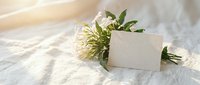 Blank cream card with white flower bouquet and green leaves on linen fabric, ideal for wedding invitations, greeting cards, and stationery design.
